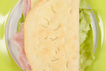 A close-up shot of a sandwich on a green plate reveals a simple filling of ham, cheese, and lettuce, emphasizing the fresh ingredients and light meal