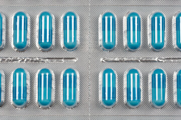 A close-up, overhead shot of multiple blister packs filled with blue capsules highlights their...