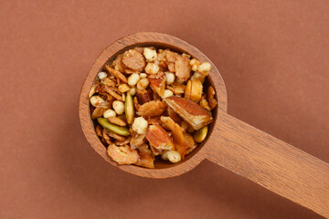 A top-down shot of a wooden spoon filled with granola shows a mix of nuts, seeds, and oats against...