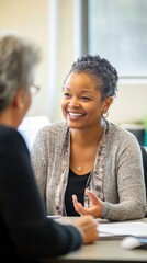 A social worker smiles warmly while discussing important matters with a client in a well-lit office. They seem to be building a supportive rapport during the meeting