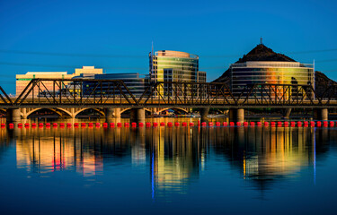 Modern office buildings and a bridge are reflected in the waters of Tempe Town Lake at dusk in Tempe Arizona
