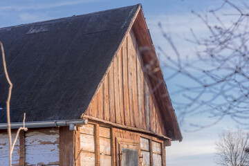 Piękny stary zabytkowy drewniany dom wiejski ze spadzistym dachem. Drewniany dom wiejski ze stromym, spadzistym dachem z ciemnych gontów. Na zewnątrz pionowe drewniane deski, zwietrzałe od starości. © Grzegorz