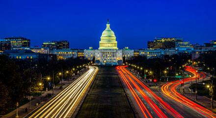 A blurred motion shot of car lights streaking through the streets, with the Washington D.C. Capitol building glowing in the background, creating a dynamic and atmospheric cityscape.