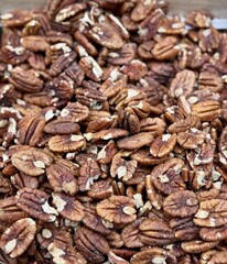 A slide of traditional caramelized, roasted, sweet pecans peeled for sale in a glass basket at a local specialty market. Close-up