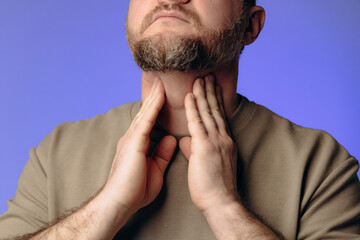 A man has a sore throat and neck due to a cold. The man holds his hand to his throat. He...