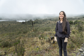 woman with backpack smiling while hiking in a foggy mountainous landscape. Dressed in a warm...