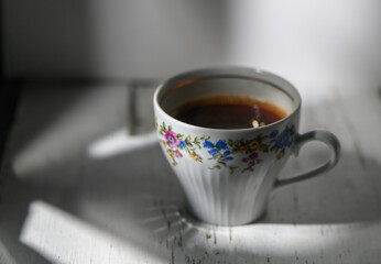 Warm coffee rests in a delicate floral cup as sunlight casts playful shadows