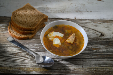 Warm bowl of hearty soup alongside fresh bread on a rustic wooden table in soft afternoon light