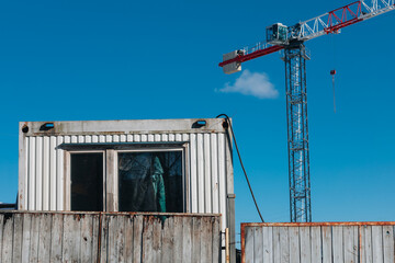 Fototapeta premium Weathered Construction Container and Tower Crane Against a Clear Blue Sky