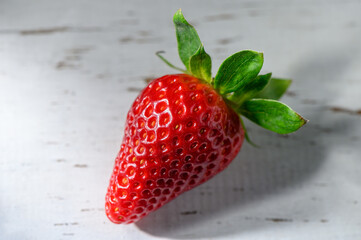 Juicy red strawberry resting gently on a rustic wooden table in soft daylight