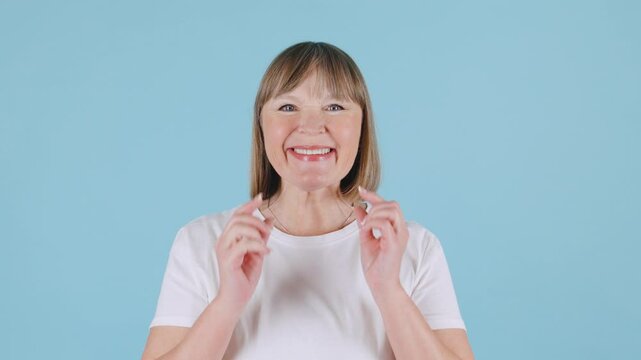 Gray-haired beautiful elderly woman doing facelift exercises, facebuilding