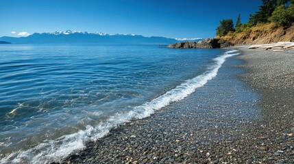Serene beach scene with clear water and distant mountains under a bright blue sky.