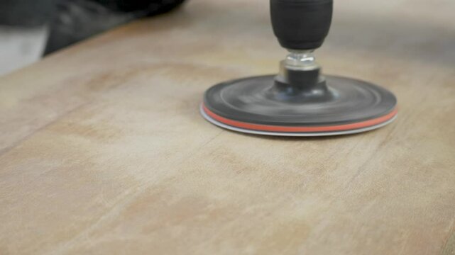 The sanding tool is working on a wooden surface, methodically reducing rough patches and preparing the wood for further processing. Power tool used to smooth surfaces by abrasion with sandpaper