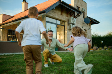 Grandchildren running to hug grandfather in backyard