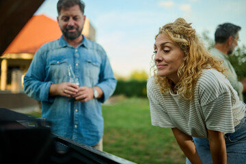 Naklejka premium Woman preparing barbecue with husband drinking beer in background