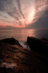 Sunrise over Buzzards Bay off the south coast of Massachusetts. This photo was taken from Gooseberry Island. It shows a wave crashing over ocean rocks while gulls fly in front of the rising sun.