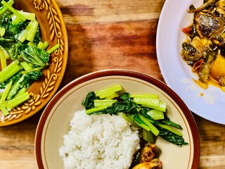 The breakfast menu is ready to be eaten on a wooden table, served on a plate is rice, pindang fish seasoned with soy sauce and stir-fried green mustard greens, cooking idea, recipe or food wallpaper