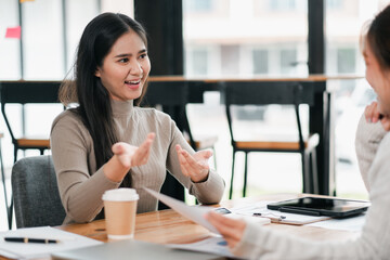 A young woman enthusiastically conversing with a colleague in a modern office setting, with coffee...