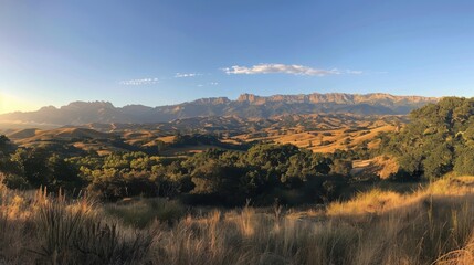 Fototapeta premium Breathtaking Panoramic View of Rolling Hills and Majestic Mountains Under a Clear Blue Sky at Sunrise