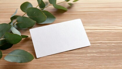 白紙のテクスチャの紙を背景にした企業用ステーショナリーの名刺　ナチュラルなユーカリの葉っぱが飾られている木製の机の上　モックアップ