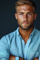 Obraz premium Young man with striking blue eyes poses confidently in a casual blue shirt against a dark backdrop