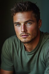 Fototapeta premium Captivating young man with striking blue eyes and relaxed expression sitting indoors during soft natural light
