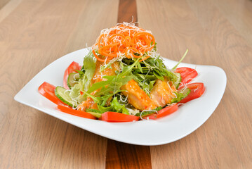 Salmon salad with mixed greens tomatoes cucumbers and shredded carrots on a white plate