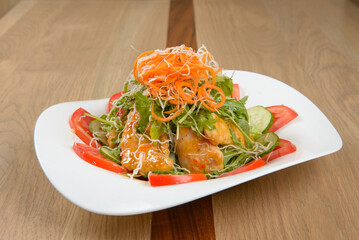 Gourmet salad with vegetables greens and protein creatively plated on a white plate and wooden surface