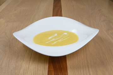 Creamy soup garnished with swirls presented in a modern white bowl atop a warm wooden table