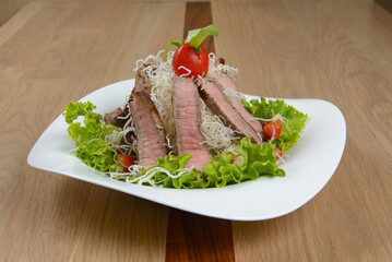 Grilled beef salad with lettuce noodles and tomato served on a white plate on a wood table