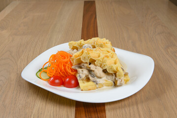 Waffle dish with creamy mushroom sauce julienned carrots tomatoes and cucumber on a square plate