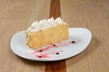Delicious cream cake: Delicate layers of pastry with soft meringue on white plate with decorational sauce