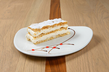 Elegant layered pastry with cream filling and powdered sugar served on a white plate Delicious treat