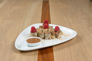 Sweet rolls dessert with caramel sauce topped with fresh raspberries and nuts on white plate