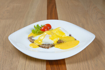 Eggs Benedict on a rustic whole grain base smothered in a vibrant creamy sauce garnished with fresh greens