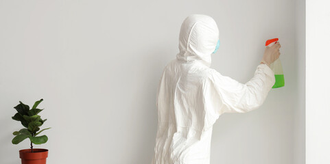 Female worker of cleaning service removing mold from wall in room, back view