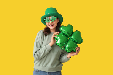 Beautiful young woman in leprechaun hat and decorative glasses with air balloon in shape of clover...