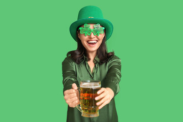 Happy young woman in leprechaun hat and decorative glasses in shape of clover with glass of beer on...