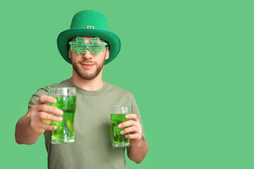 Young man in leprechaun hat with glasses of beer on green background. St. Patrick's Day celebration