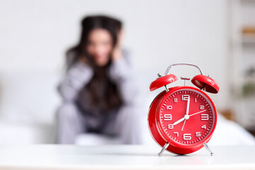 Red alarm clock on table against stressed woman sitting in bedroom, closeup