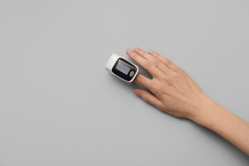 Female hand with pulse oximeter on grey background