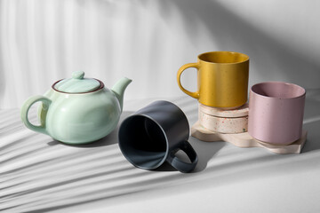Different ceramic mugs, teapot and plaster stand on white background