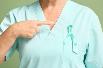 Mature female doctor with teal ribbon on green background, closeup. Cervical Health Awareness Month