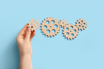 Hand with wooden gears on light blue background