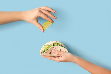 Female hands with lime and tasty fresh taco on blue background