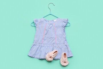 Hanger with stylish baby dress and booties on color background