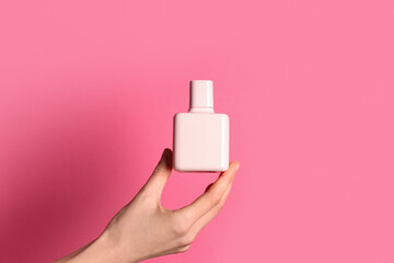 Female hand with bottle of perfume on pink background