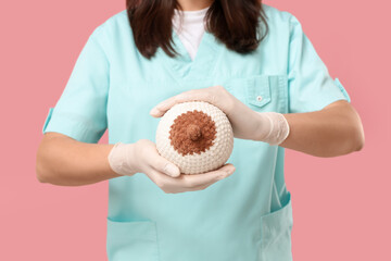 Female doctor with knitted breast model on pink background, closeup