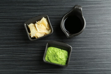 Hot wasabi paste, soy sauce and ginger on black textured table, flat lay