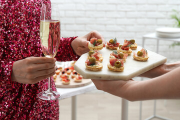 Woman taking tasty canape from waiter with board indoors, closeup